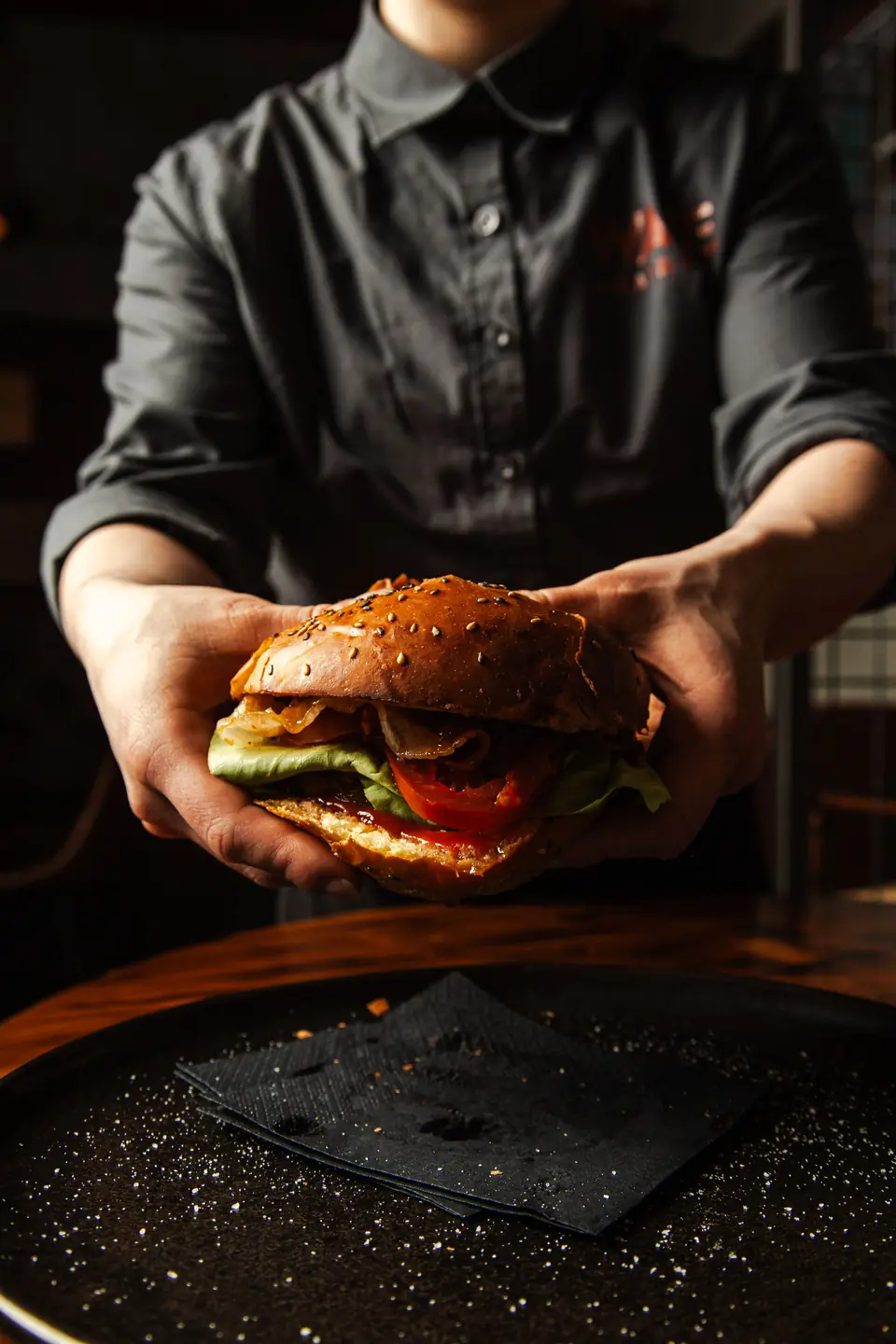 Chef in divisa scura che presenta un hamburger gourmet