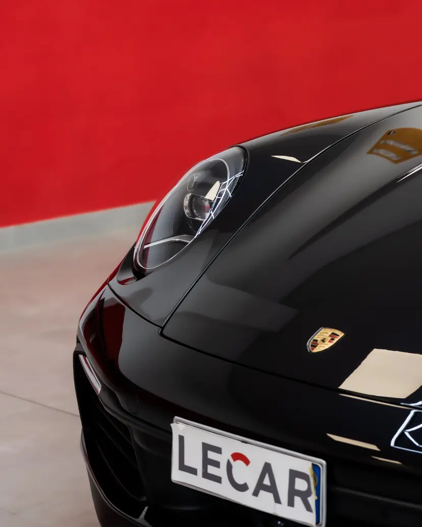 Frontale di una Porsche 911 nera con faro tondo, su fondo rosso