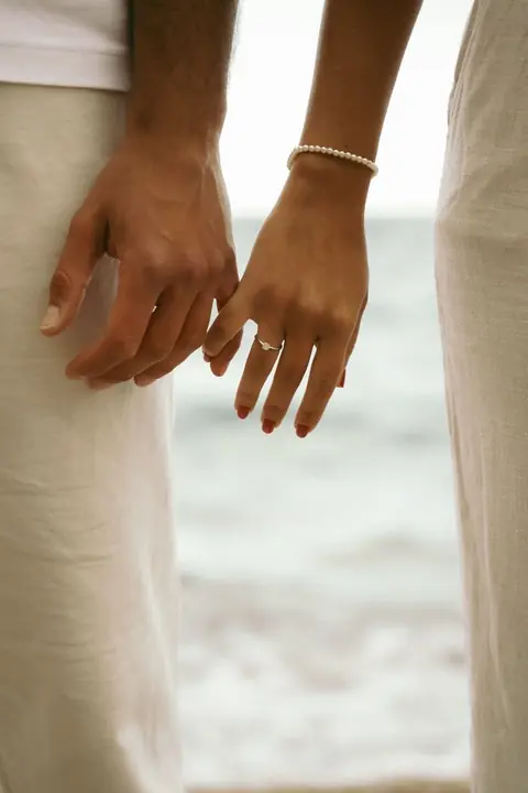 Mani di una coppia in riva al mare, lei con l'anello di fidanzamento